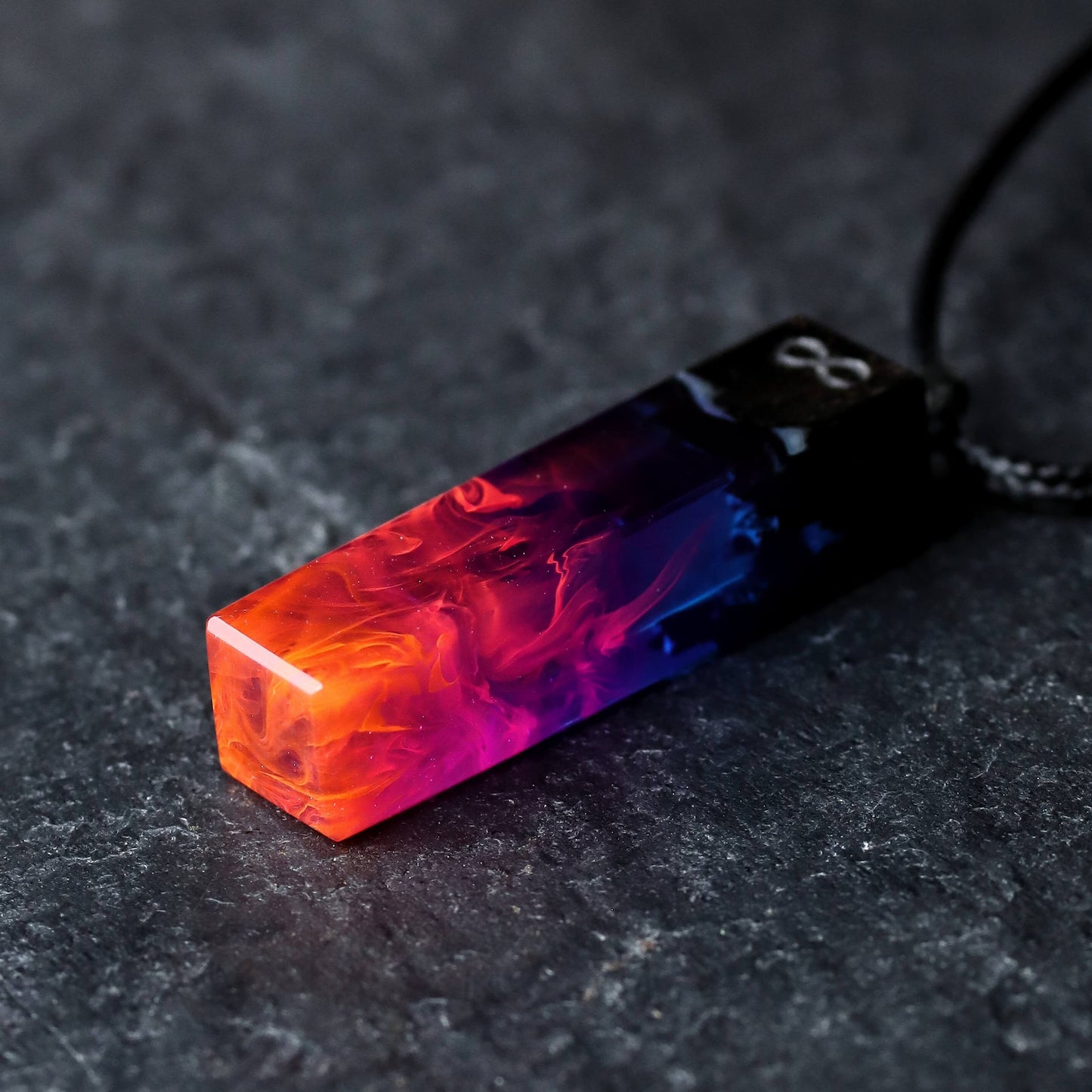 Wood resin necklace with fire and nebula design inside a fang-shaped pendant, orange and purple handmade jewelry on black cord