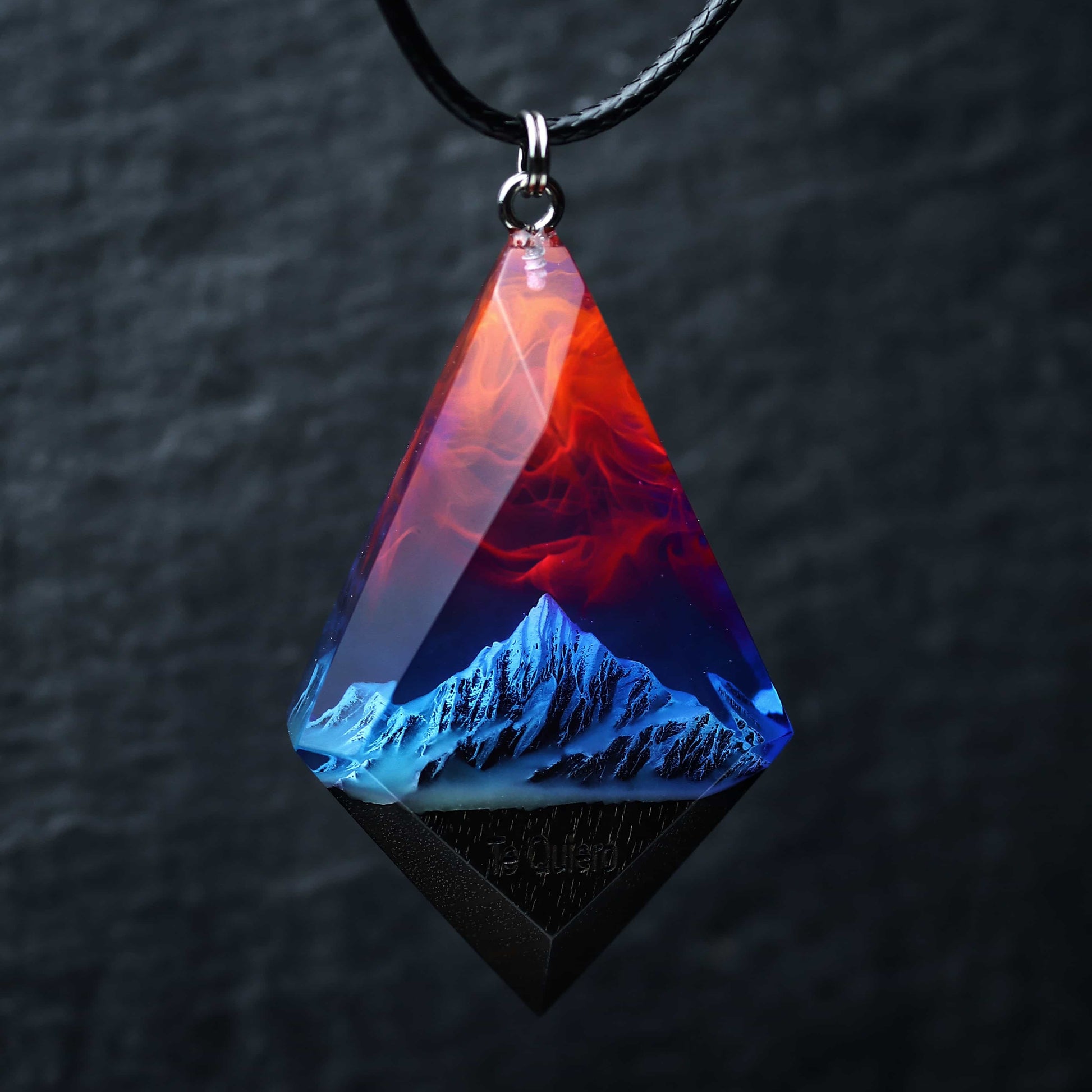 Wood resin necklace with fire and nebula sky over blue snowy mountains, faceted rhombus pendant held in hand, handmade jewelry