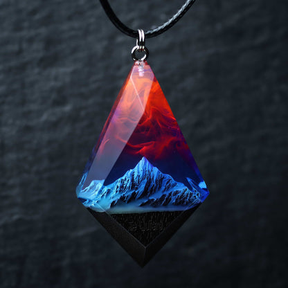 Wood resin necklace with fire and nebula sky over blue snowy mountains, faceted rhombus pendant held in hand, handmade jewelry