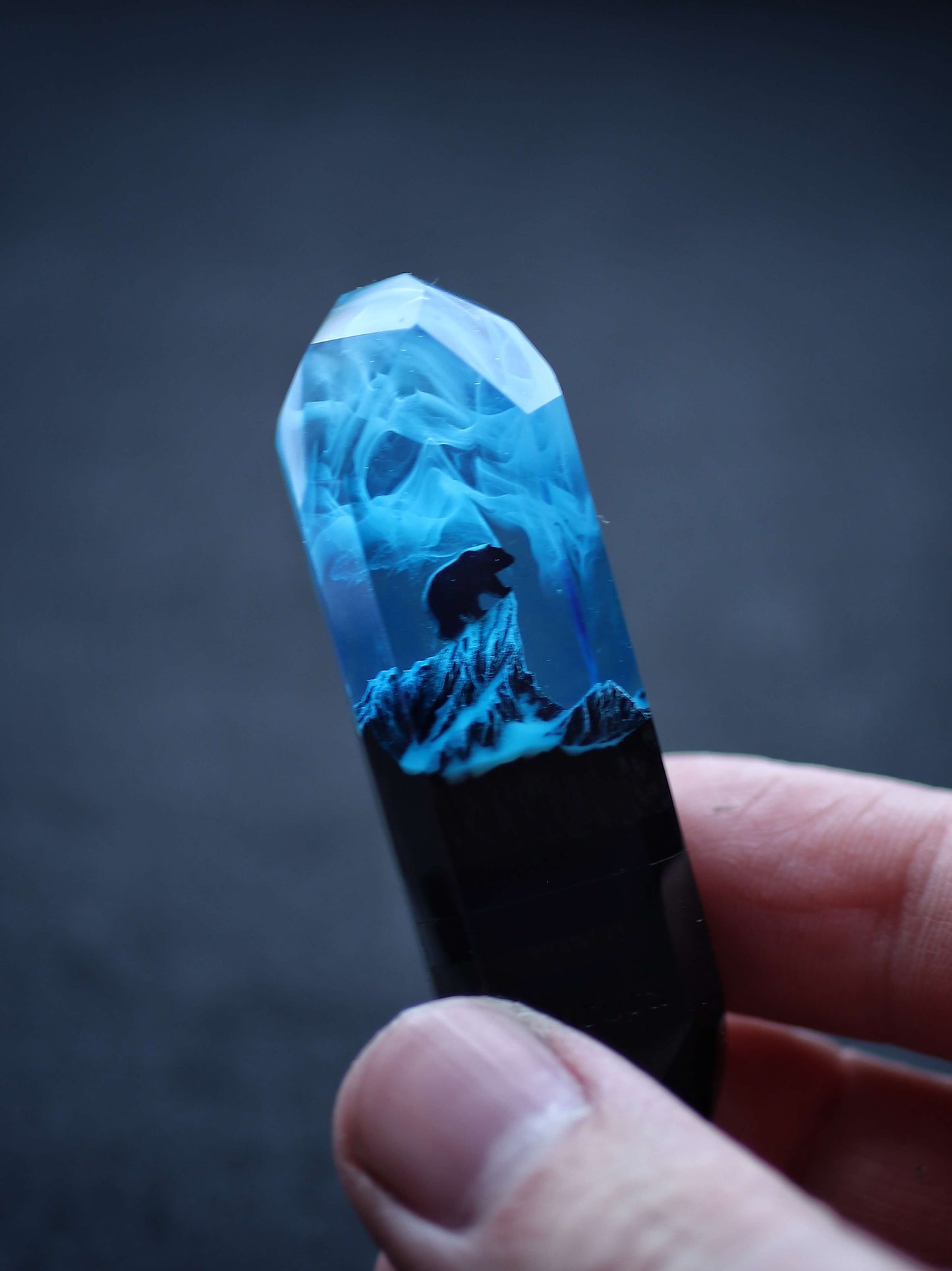Blue crystal with a mountain scene inside held by a hand against a dark background