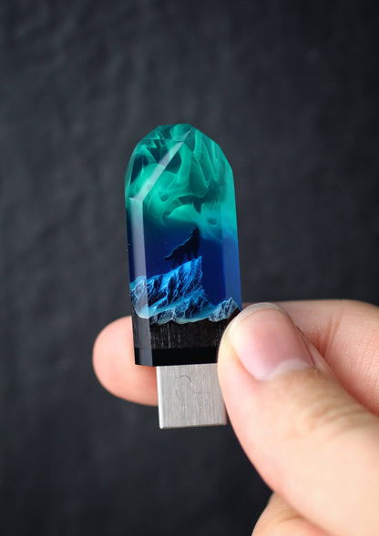 Hand holding a USB drive with a blue and green design against a dark background