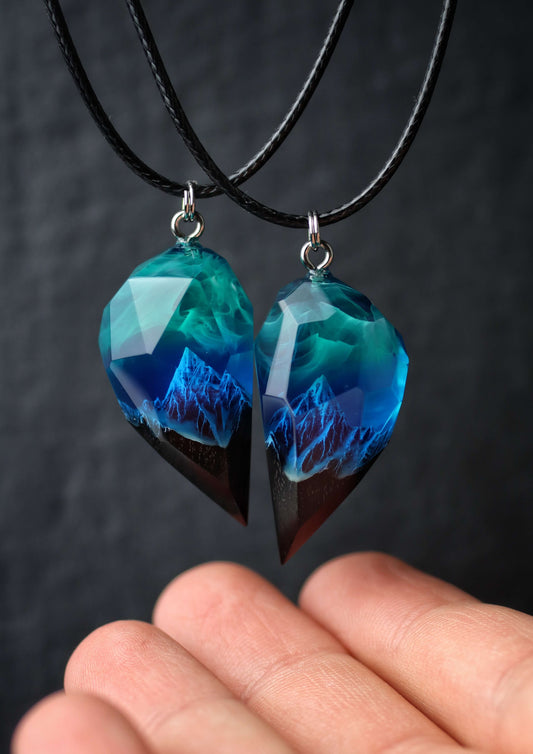 Hand holding handmade resin and wood couple pendants with mountain scene