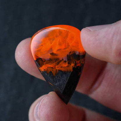 Fire wood resin guitar pick held between fingers for size reference