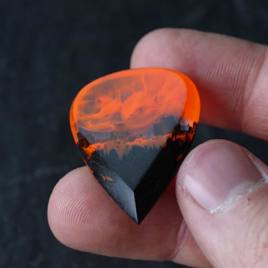 Fire wood resin guitar pick held between fingers for size reference
