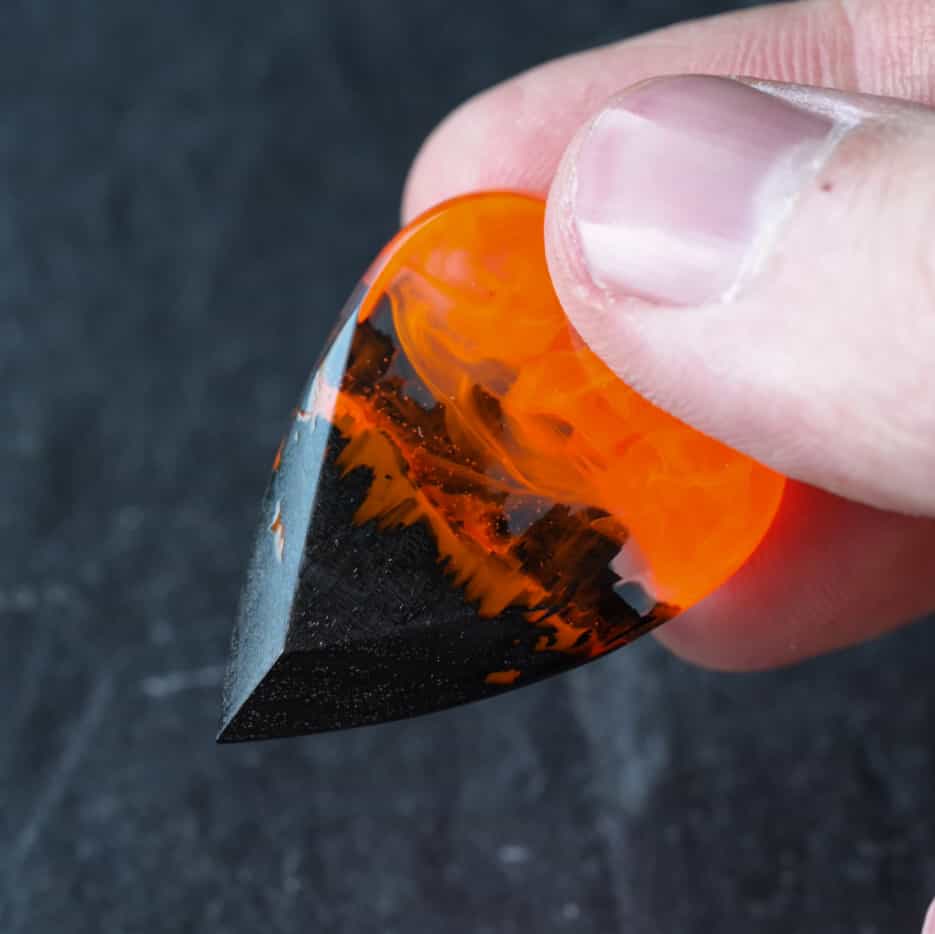 Fire wood resin guitar pick held between fingers for size reference