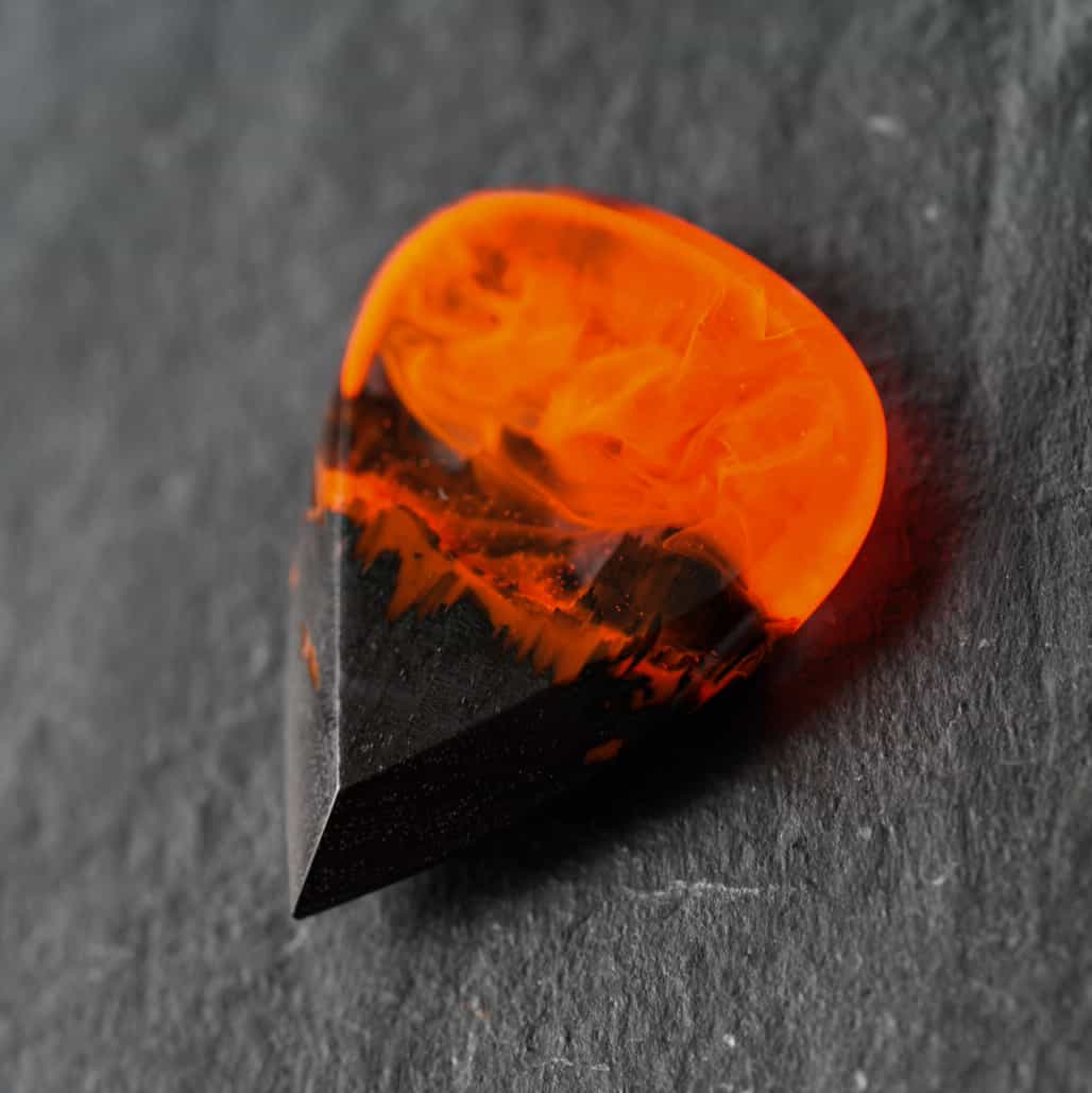 Handmade fire guitar pick made of black hornbeam wood and epoxy resin, close-up on dark stone