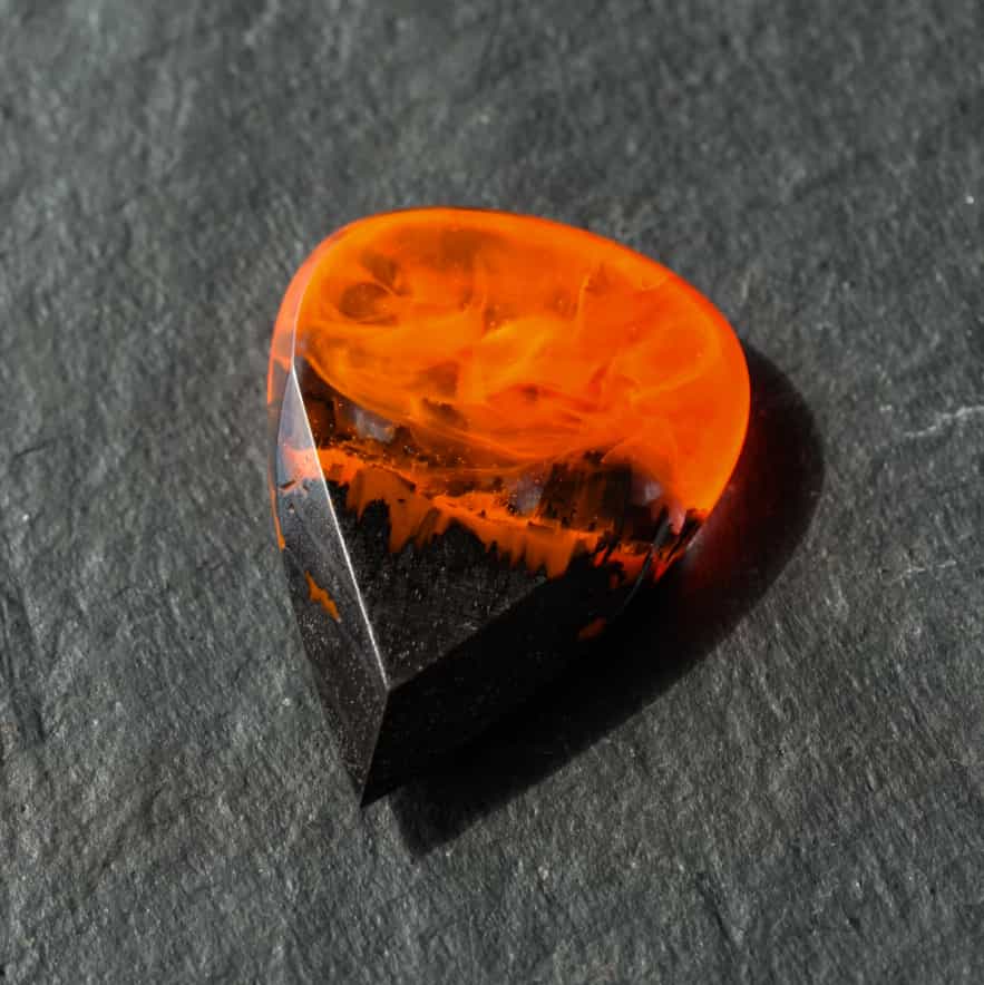 Handmade fire guitar pick made of black hornbeam wood and epoxy resin, close-up on dark stone