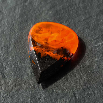 Handmade fire guitar pick made of black hornbeam wood and epoxy resin, close-up on dark stone