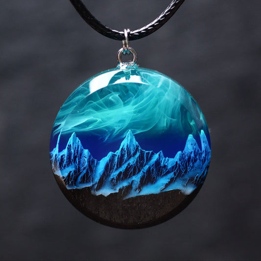Wood resin necklace with northern lights over snowy mountains inside a round pendant, handmade glow jewelry on black cord