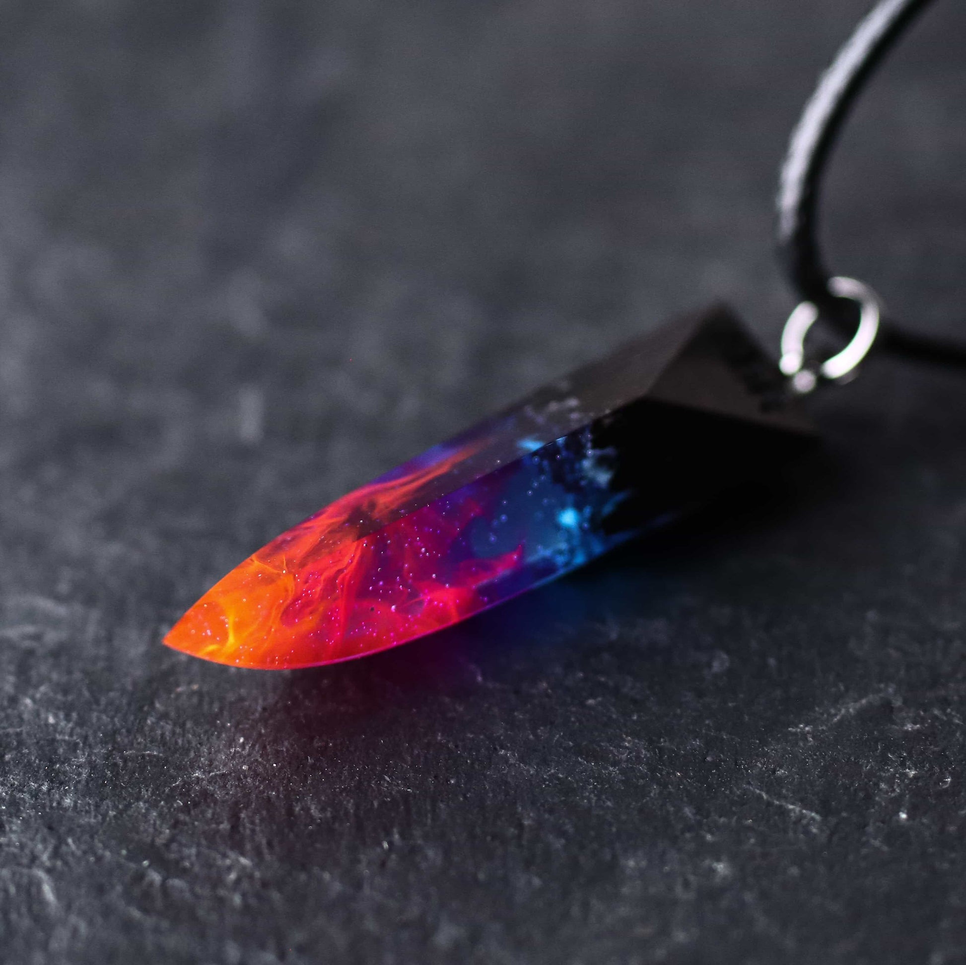 Wood resin necklace with fire and nebula design inside a fang-shaped pendant, orange and purple handmade jewelry on black cord